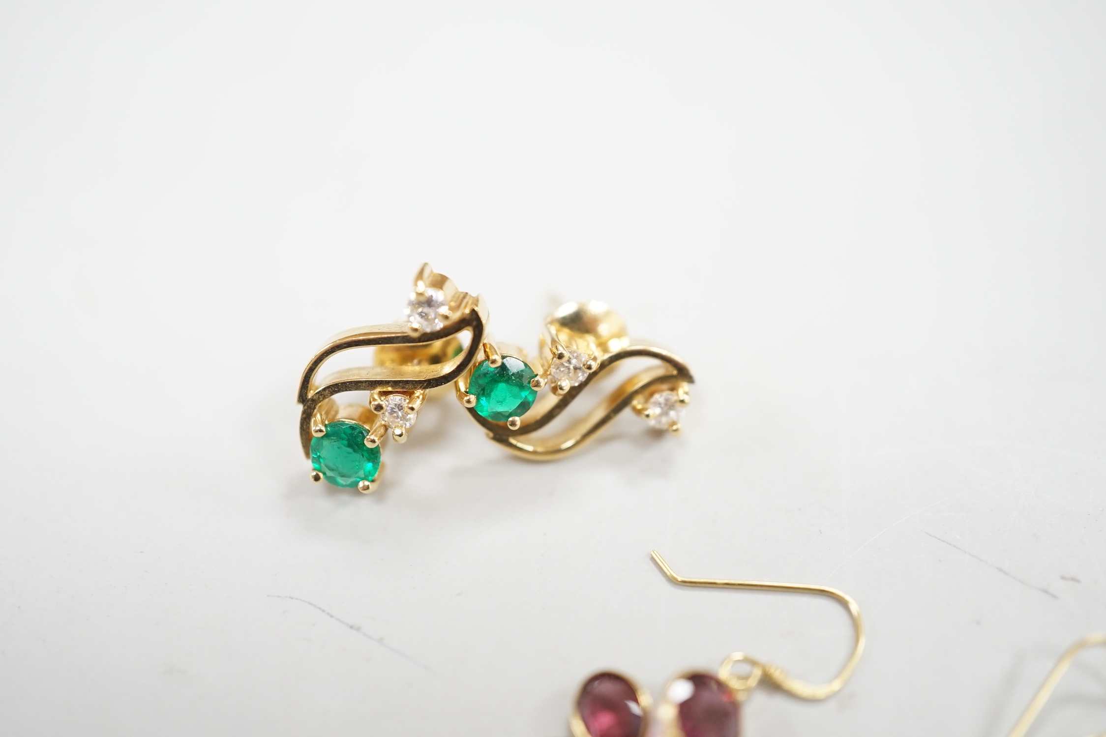 A modern pair of yellow metal, emerald and diamond set three stone ear studs, 14mm and a modern pair of yellow metal and garnet cluster set drop earrings, gross weight 8.3 grams.